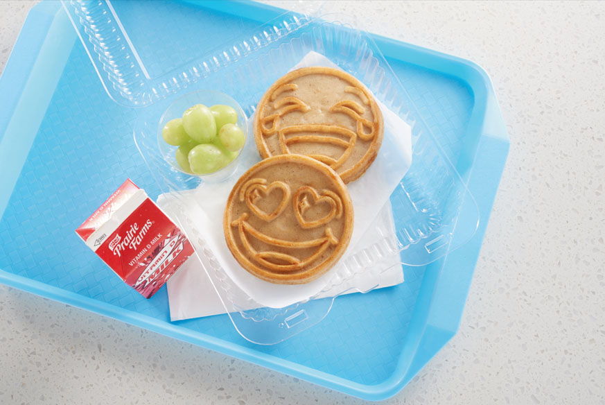 2 Eggo products on a cafeteria tray with grape and a carton of milk